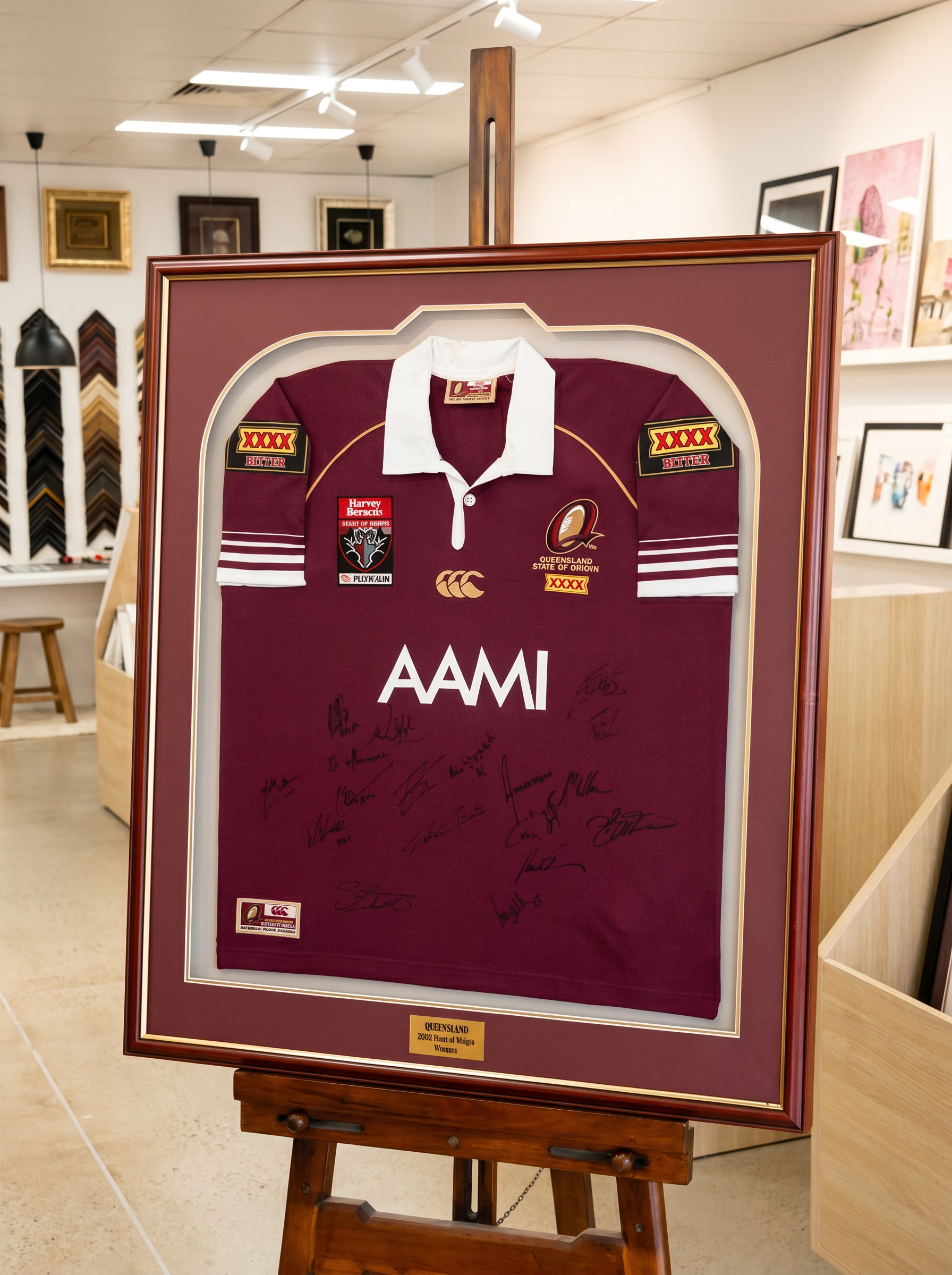 Framed maroon sports jersey with signatures on a wooden easel in an art gallery.
